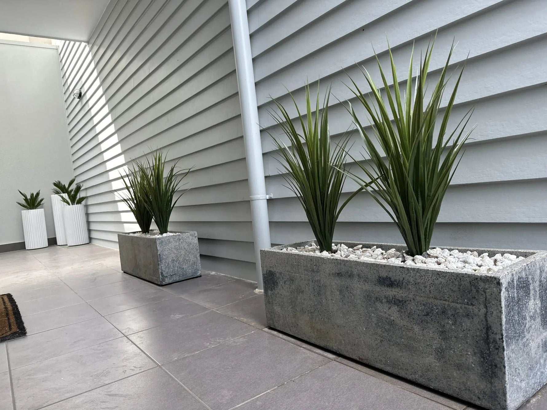 Decorative planters with plants against a gray siding wall.
