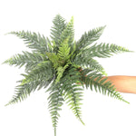 Artificial fern plant held by a hand on a white background