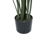 An artificial green plant with long, slender leaves in a matte black cylindrical pot filled with gray faux soil, shown against a plain white background.
