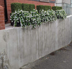 Artificial plants and flowers arranged on a concrete ledge with a brick wall background.
