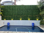 Pool area with green artificial hedge wall and blue decorative vases.