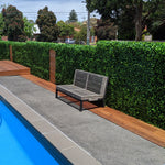 Gray outdoor bench by a pool with green hedges and trees in the background
