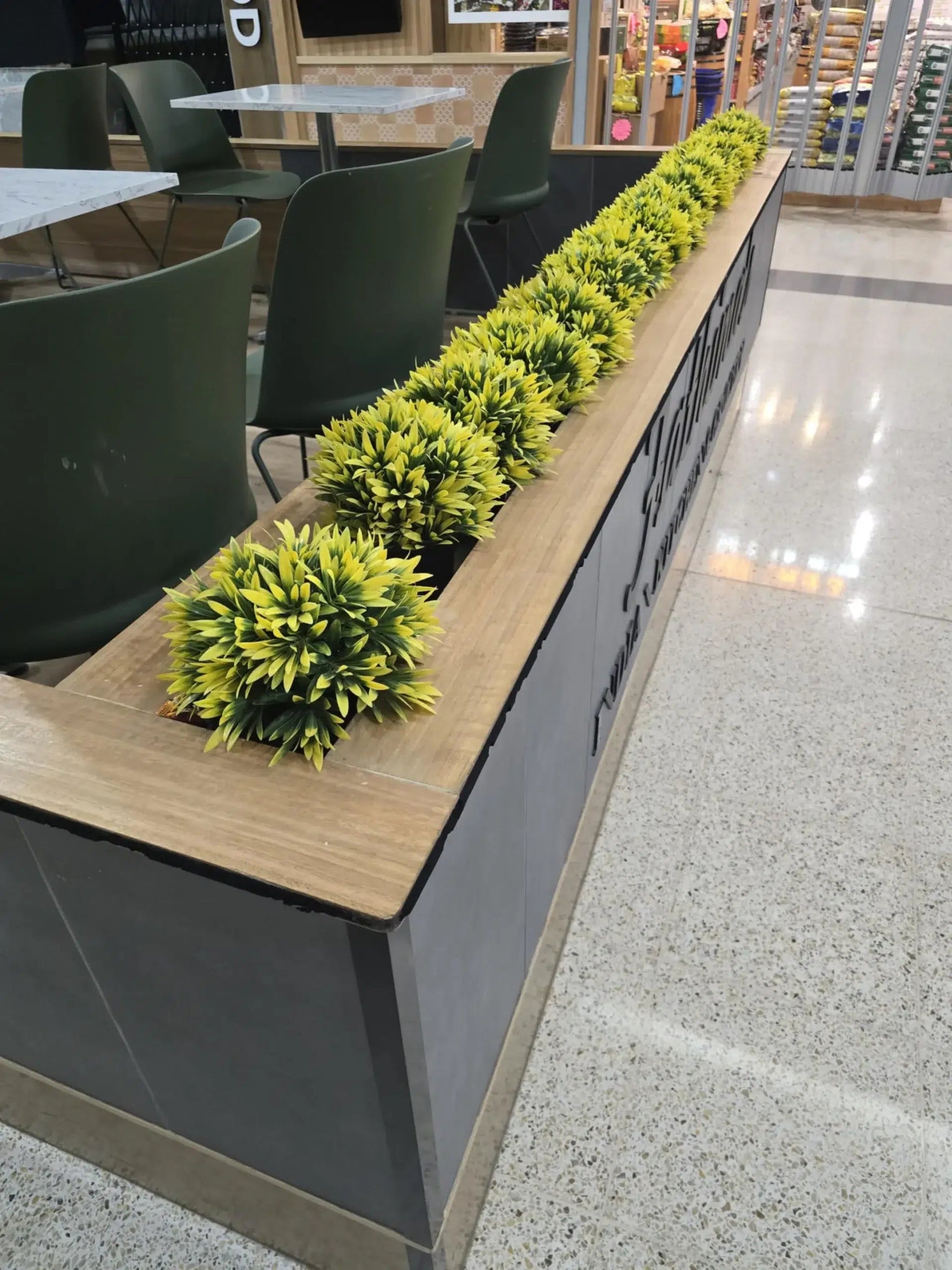 Long wooden counter with green artificial plants in a modern indoor setting