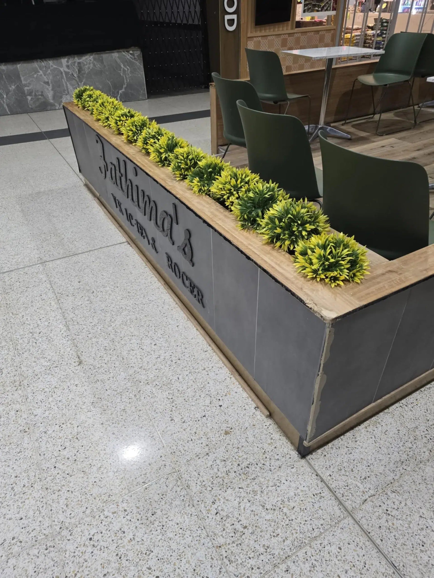 Decorative planter with green plants in an indoor setting, featuring a brand name.