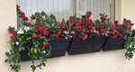 Row of black planters with artificial flowers on a wall