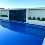 Modern pool with water feature and planters against a clear blue sky