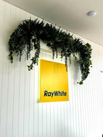 Ray White sign with green foliage decoration on a white wall